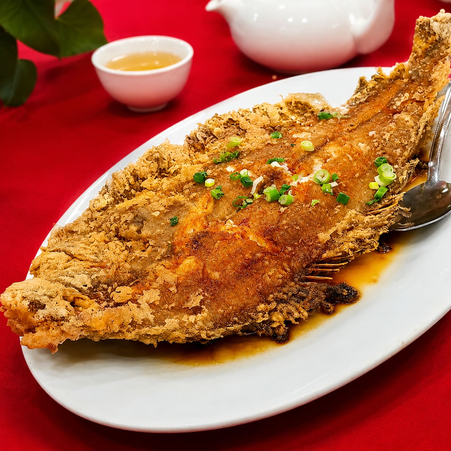 A whole flatfish, deep-fried golden and scored across the body, on an oval platter in a dark soy sauce with spring onion.