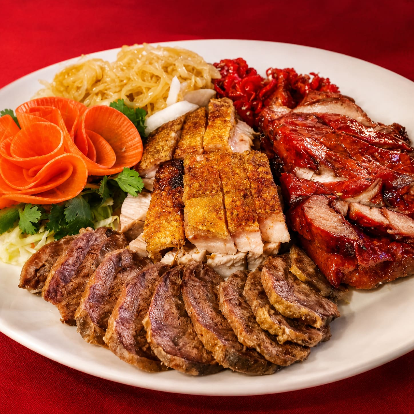 A combination platter of sliced roast duck, crackling pork belly and char siu arranged in rows with carved carrot flowers and shredded garnish.